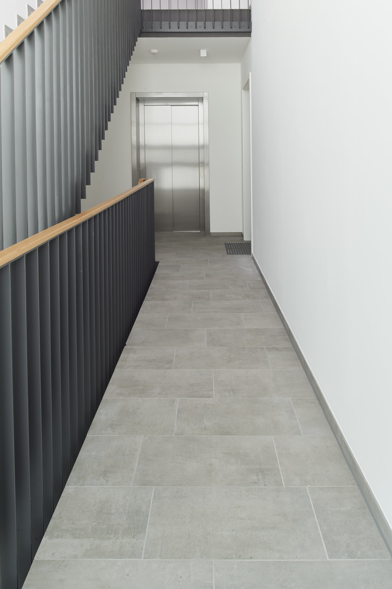 Grey porcelain tiles in a modern hallway with stairs and an elevator.