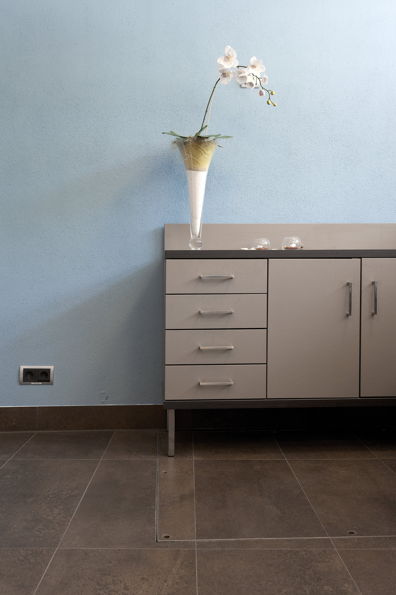 Modern, dark floor tiles in a stylish interior with a sideboard and blue wall.