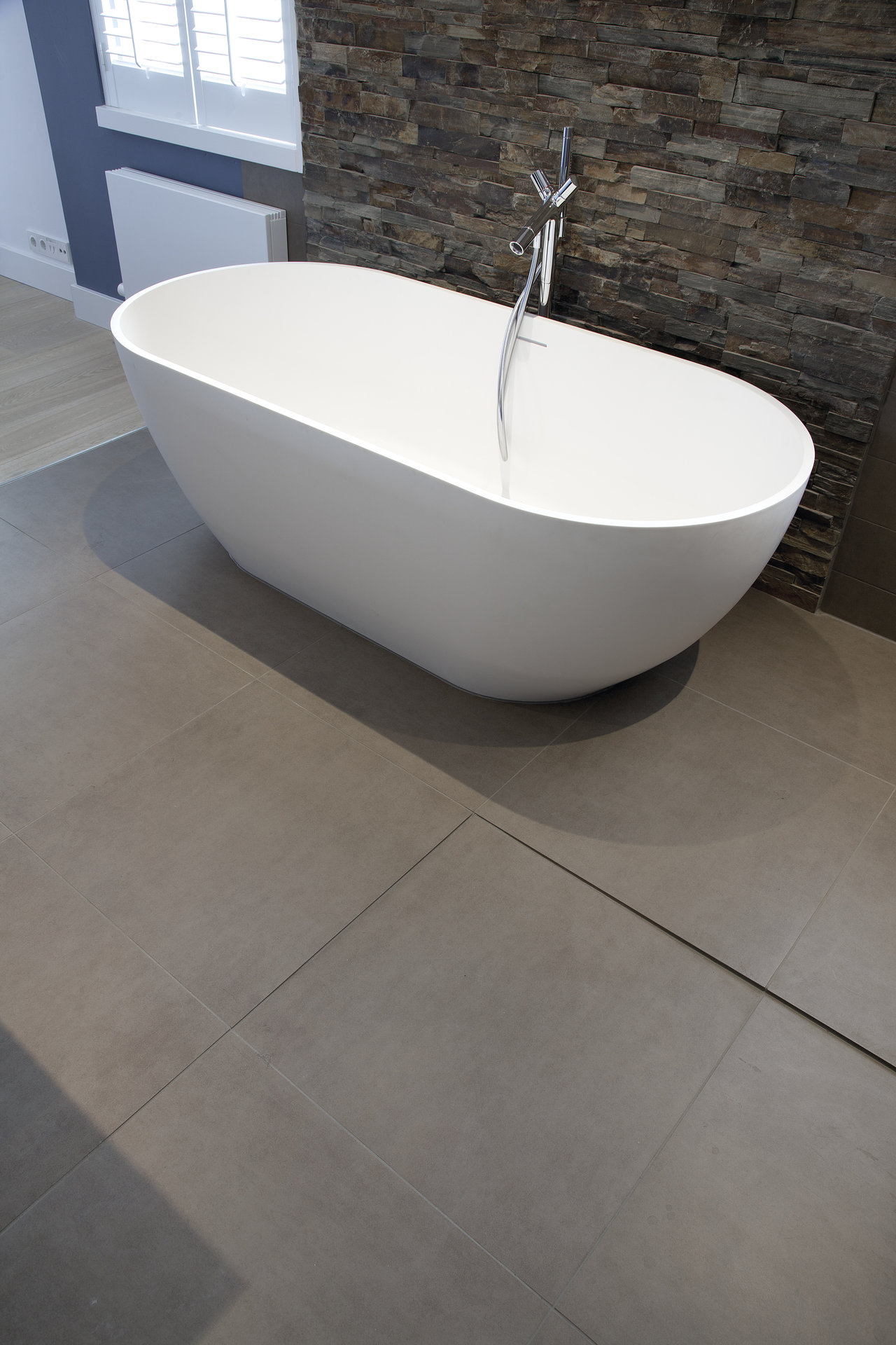 Modern bathroom with large grey floor tiles and a textured stone-effect accent wall.