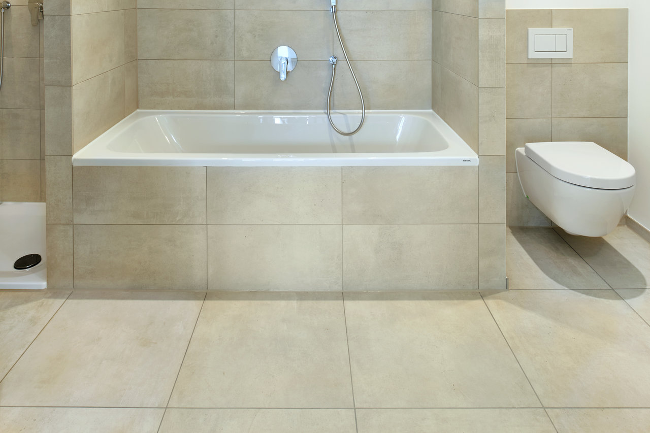 Light, large-format bathroom tiles with bath and WC.
