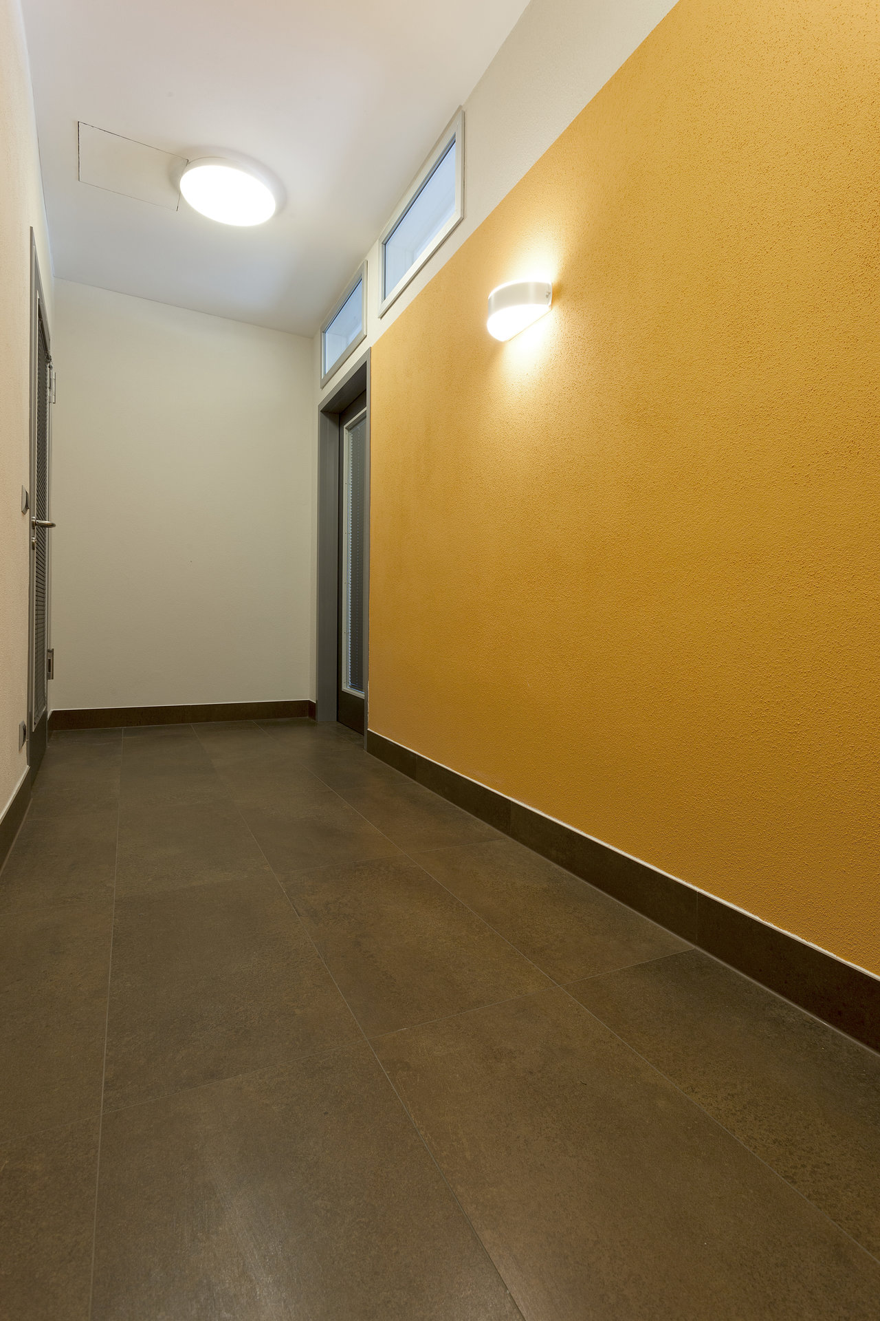 Modern hallway with large-format, dark grey floor tiles and a yellow accent wall.