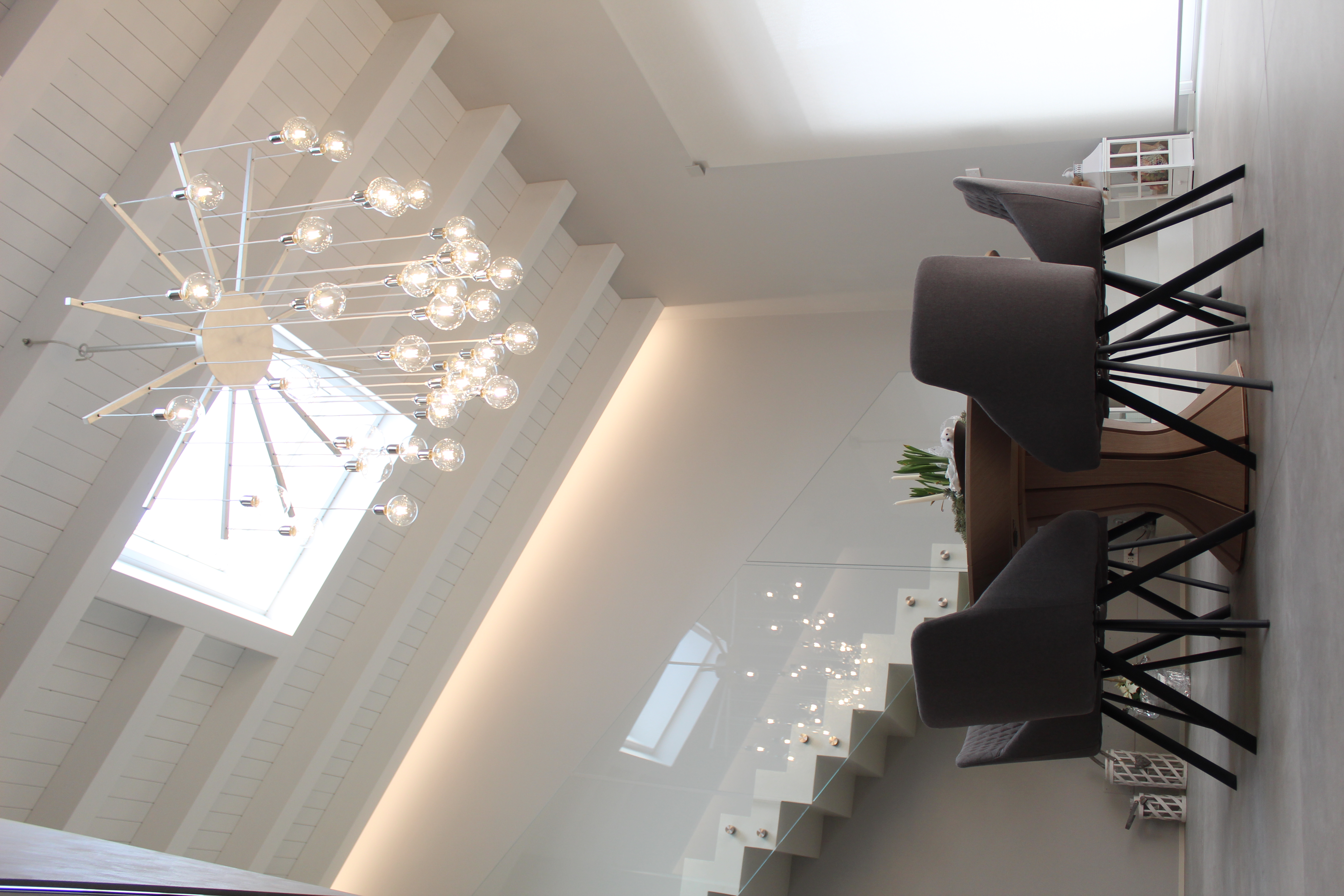 Modern dining area with light tiles, wooden ceiling, and designer chandelier.