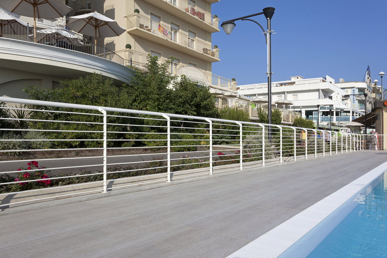 Premium grey outdoor tiles by the pool, with white railing and buildings in the background.