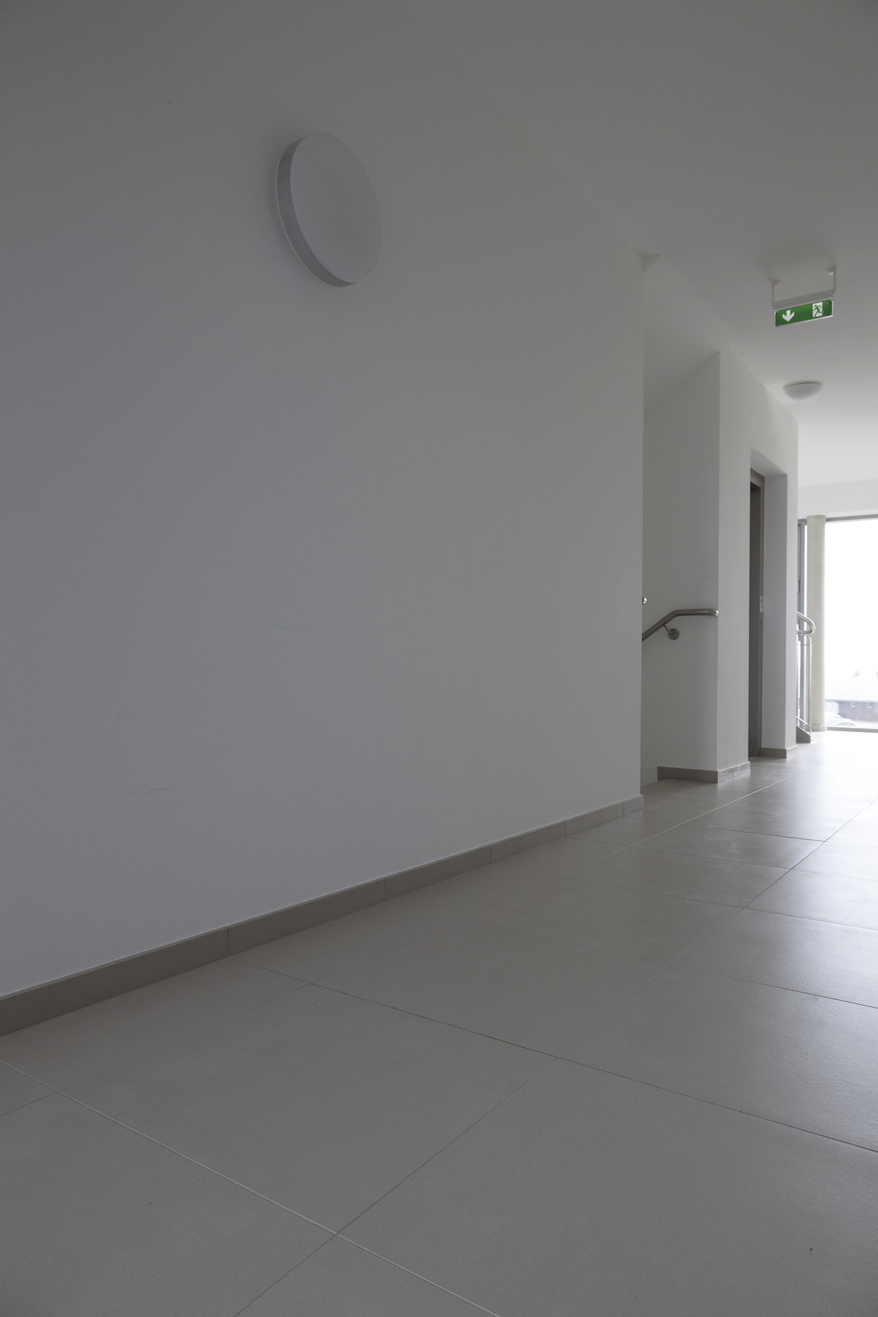 Bright, modern hallway with large-format, light grey floor tiles and matching skirting.
