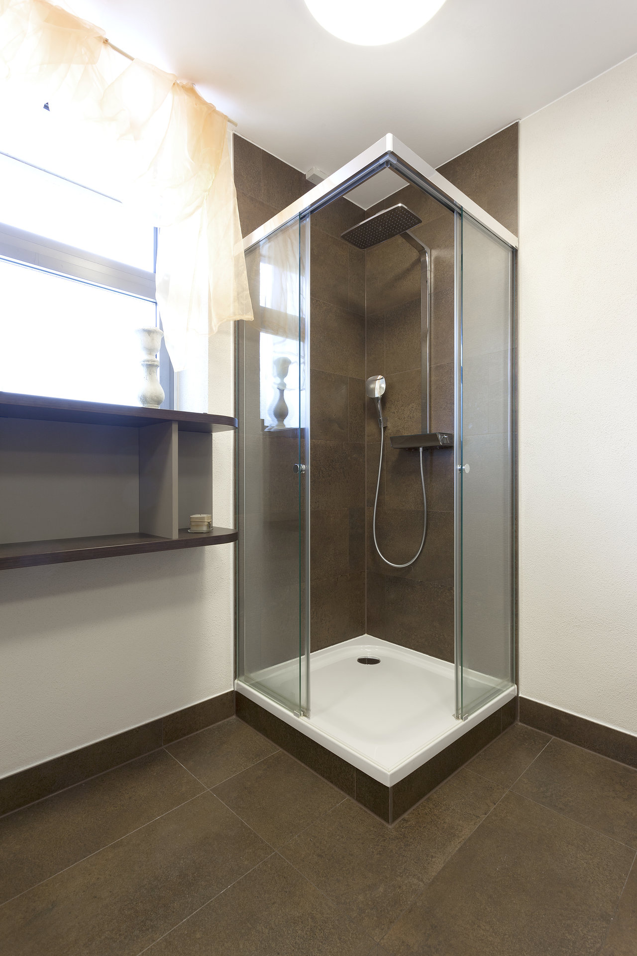 Stylish bathroom with dark brown tiles on floor and shower wall.