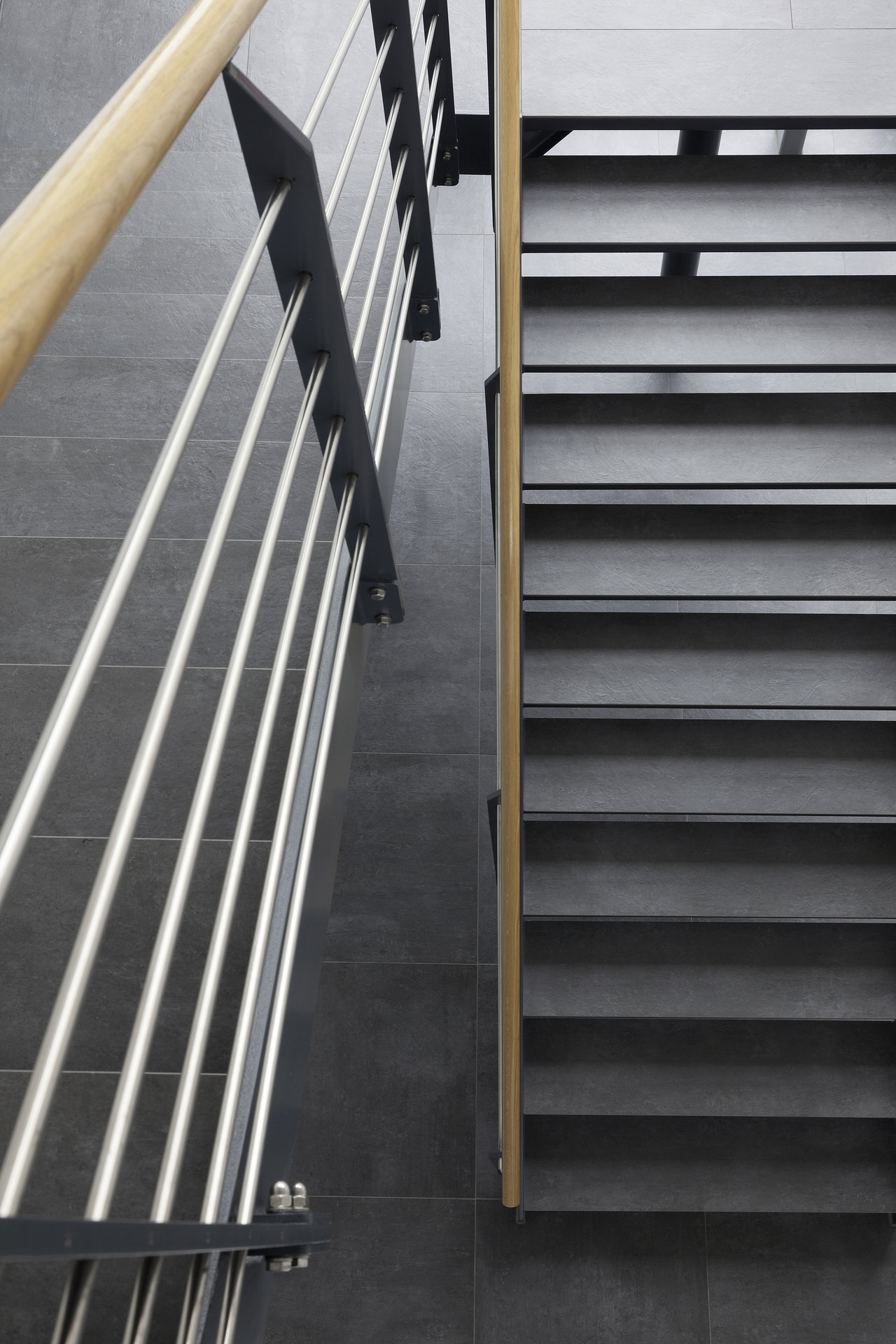 High-quality dark grey tiles on modern stairs and floor with elegant railing.