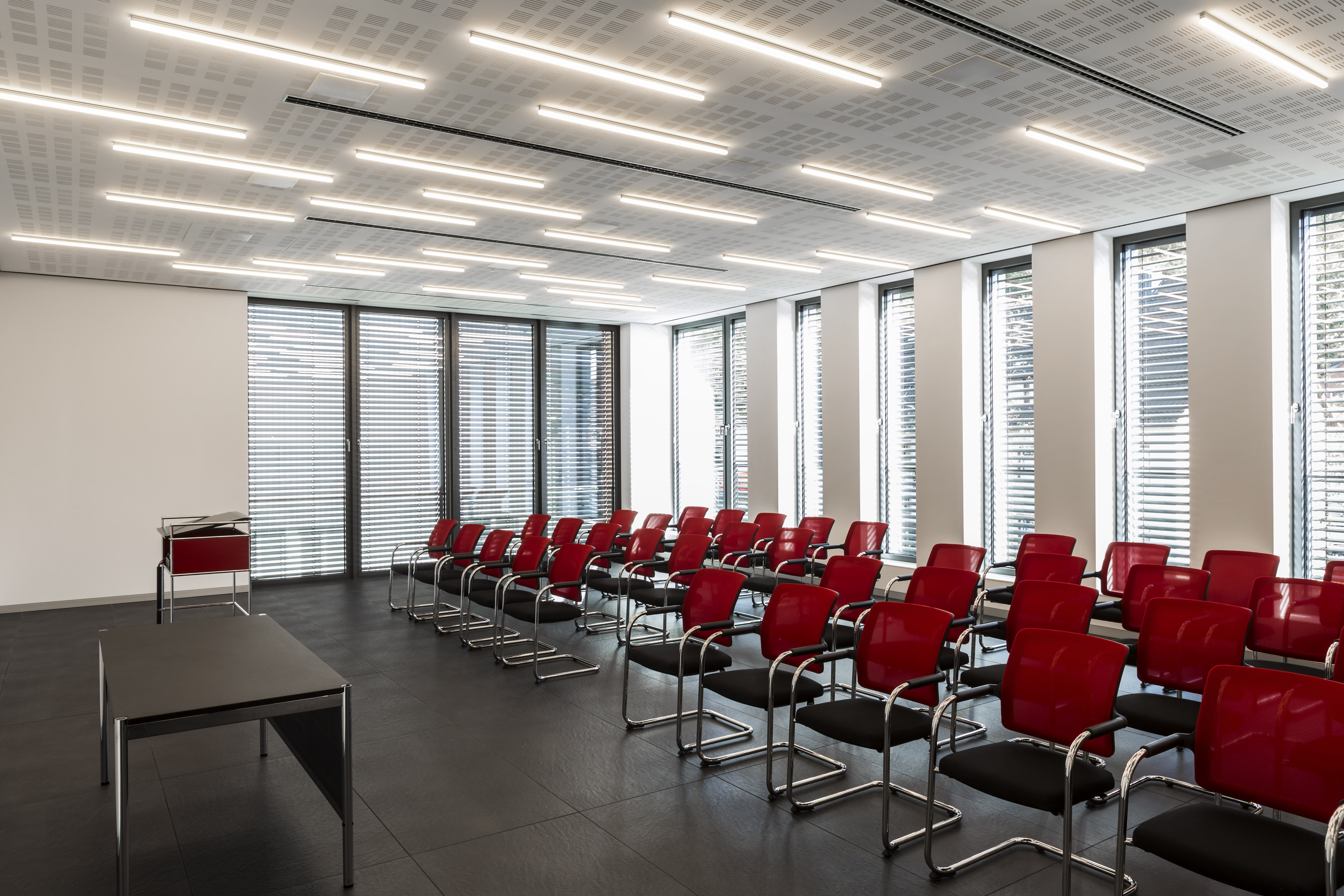 Modern conference room with dark tiles and rows of red chairs.