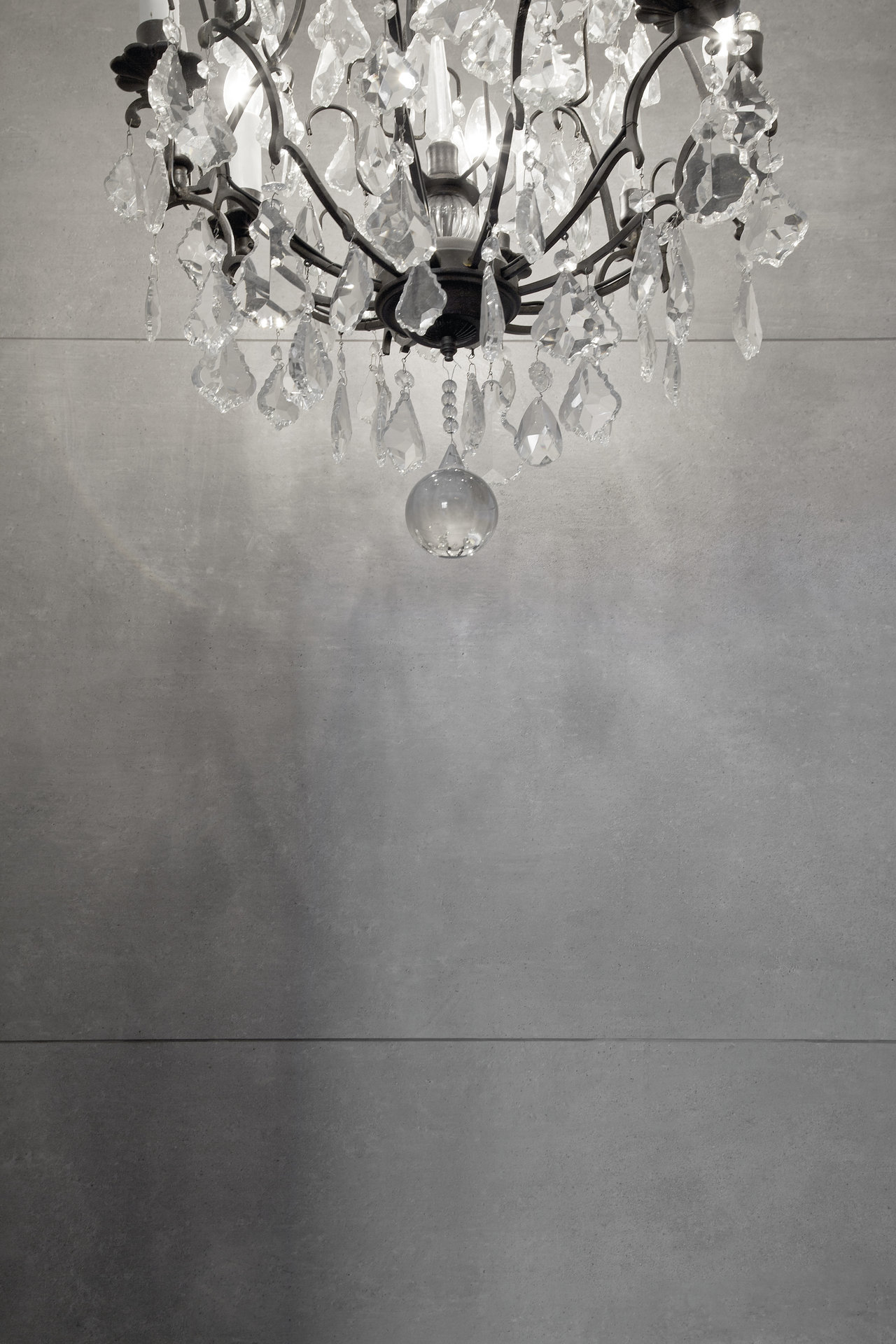 Crystal chandelier casts light reflections on modern, large-format wall tiles.
