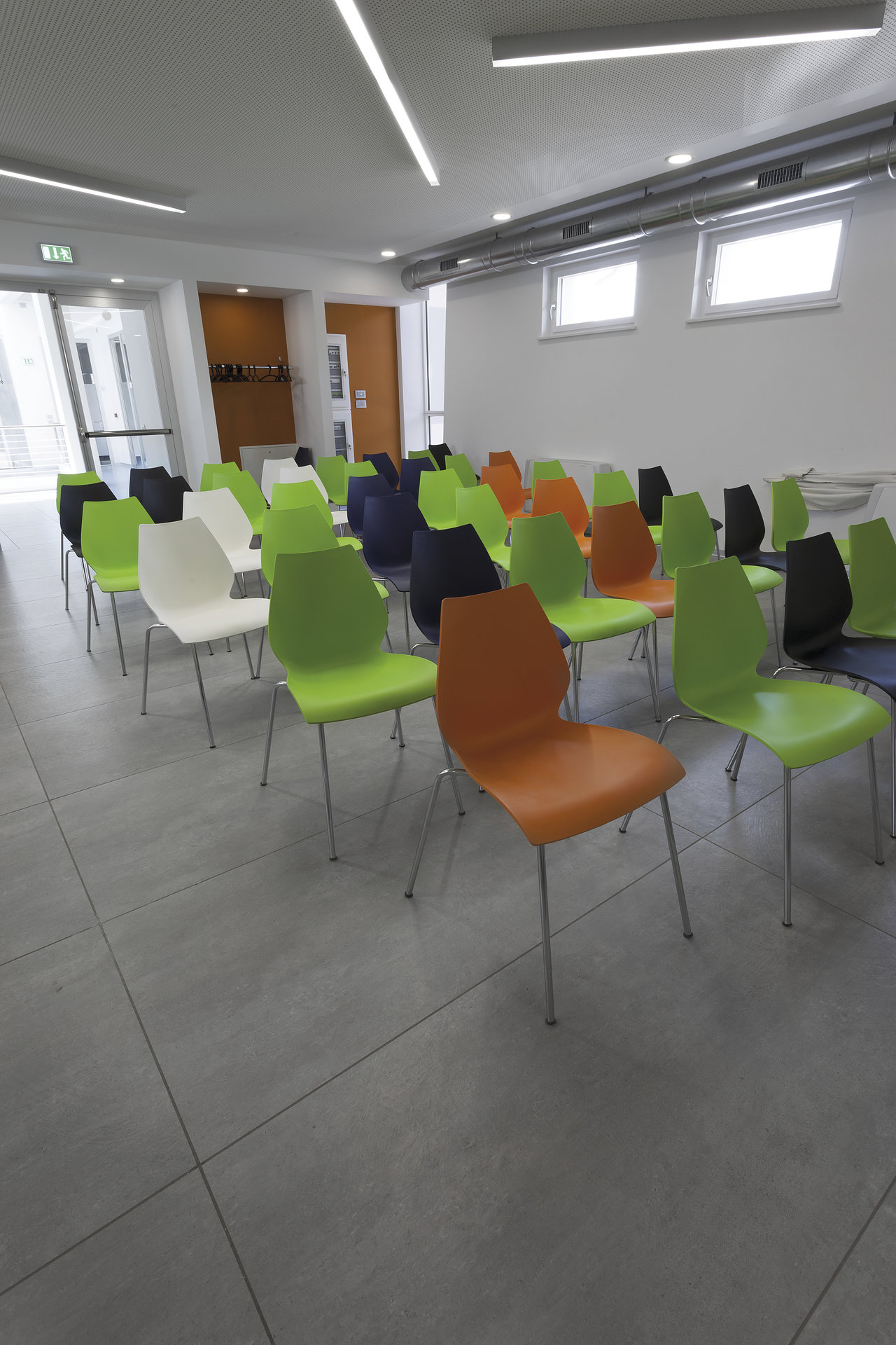 Large-format, light grey tiles in the conference room with colourful chairs.
