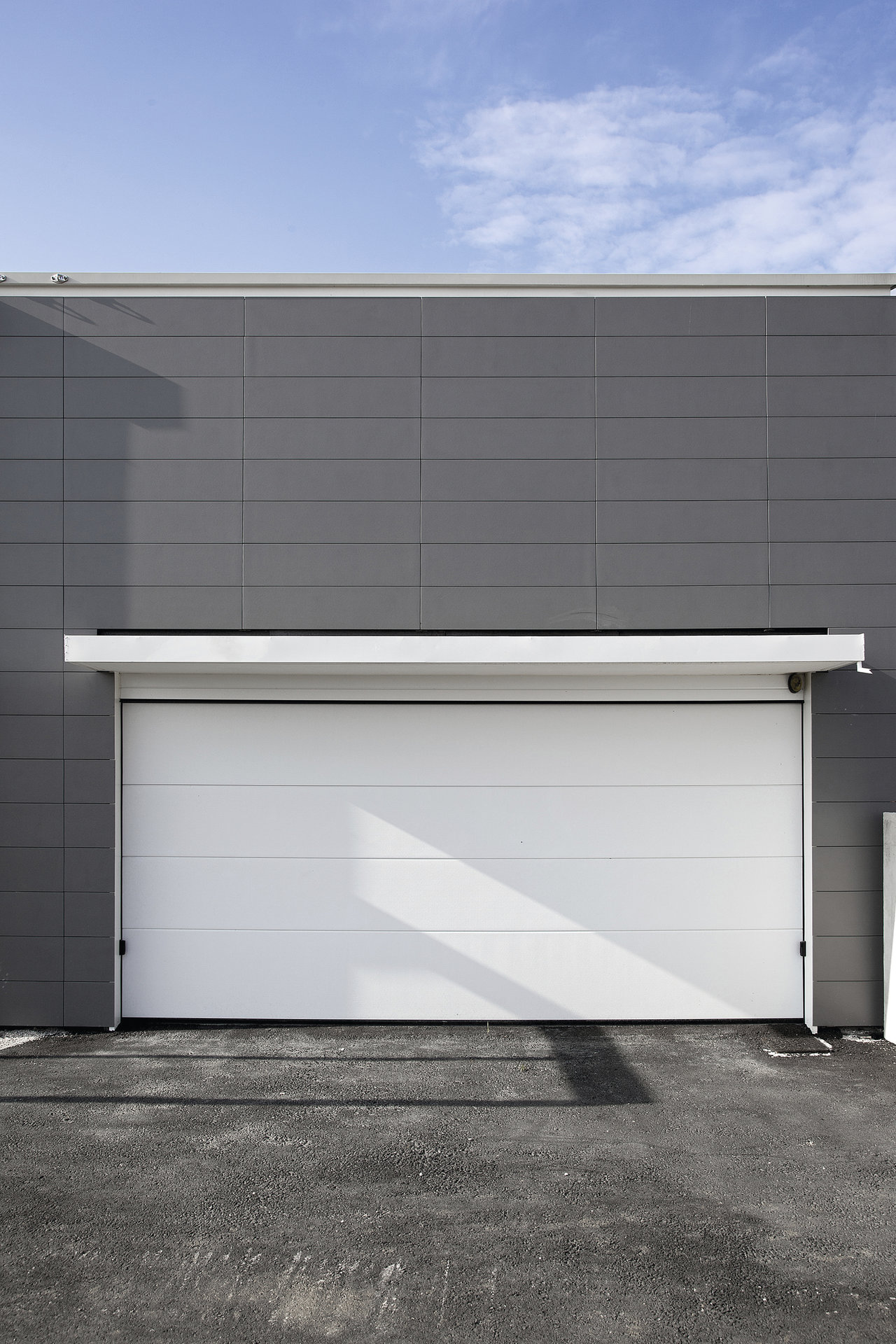 Building facade with white sectional door and grey tiles.