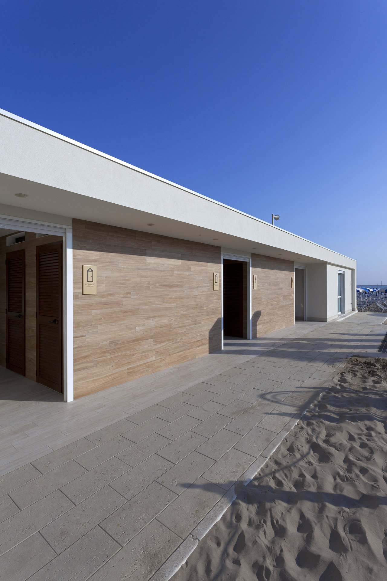 Modern outdoor tiles for paths and facades, shown at the beach with light slab path and wood effect.