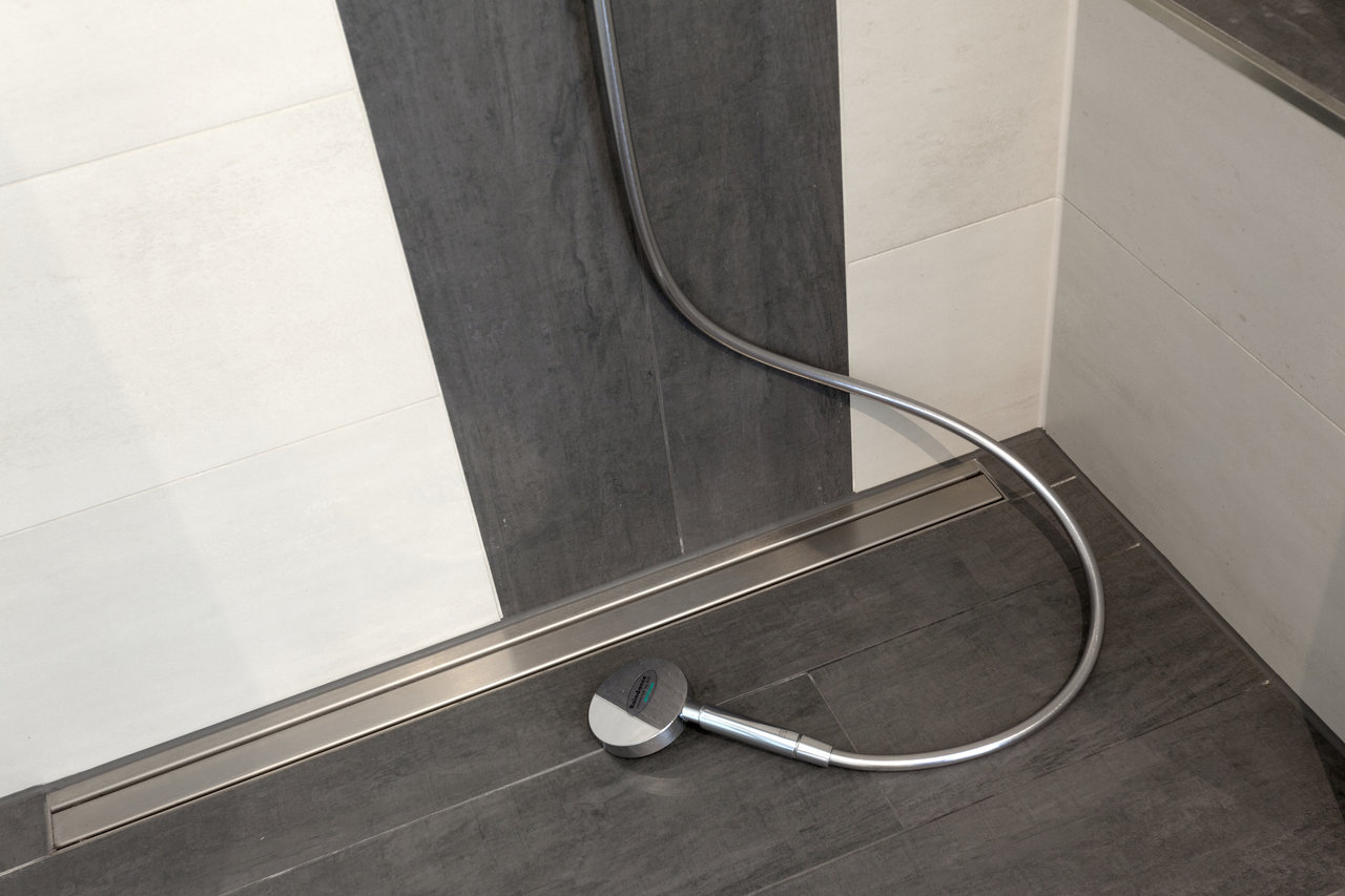 Modern shower with dark floor tiles, white-grey wall design and elegant linear drain.