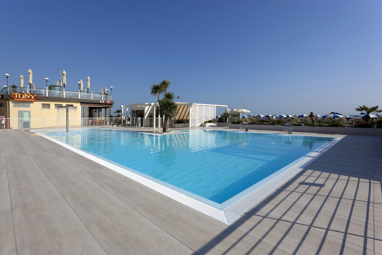 Modern grey outdoor tiles around a sunny pool area with a restaurant and sea view.