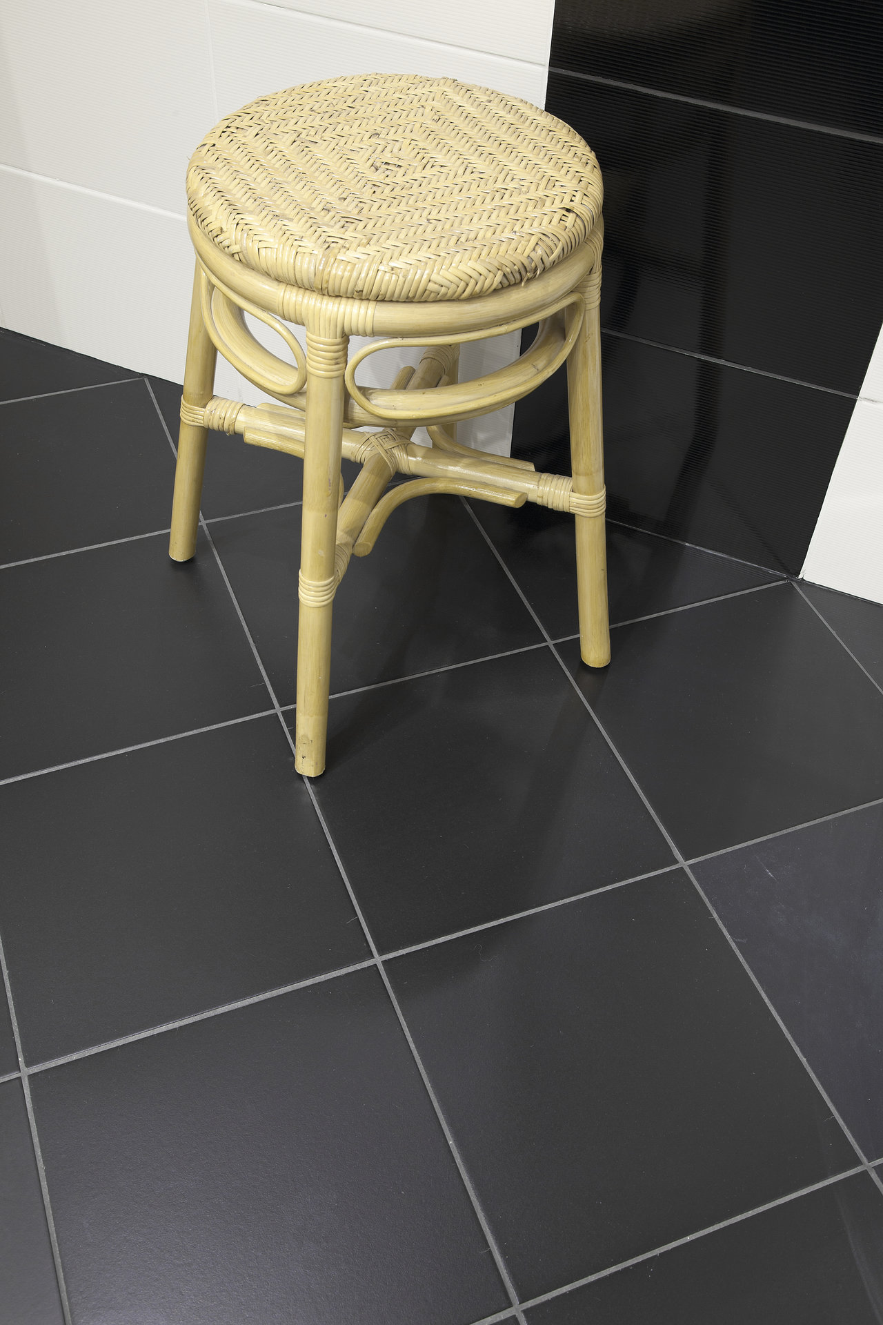 Anthracite square floor tiles with light grout and rattan stool.