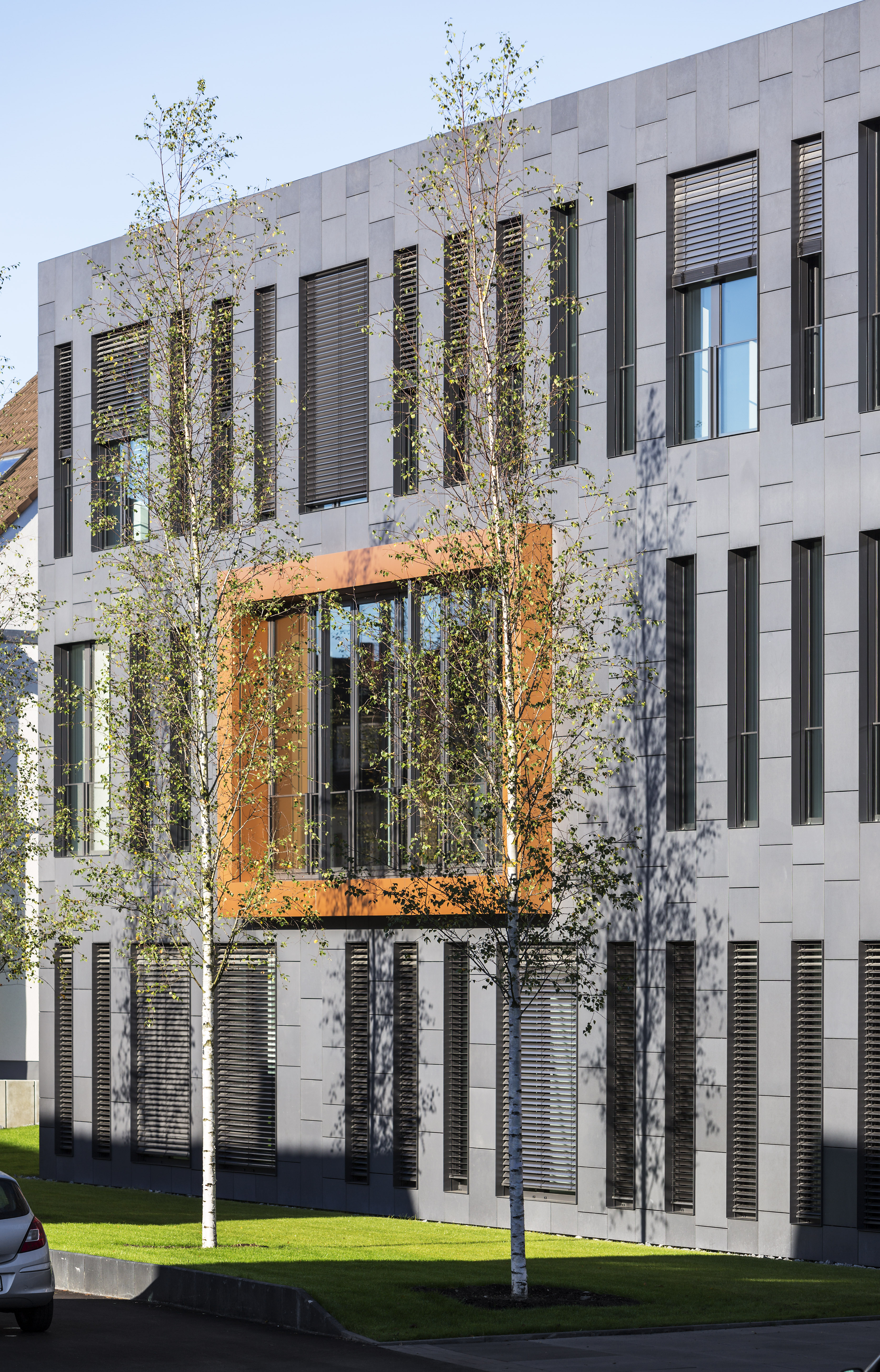 Modern grey-tiled facade with a distinctive window and trees.
