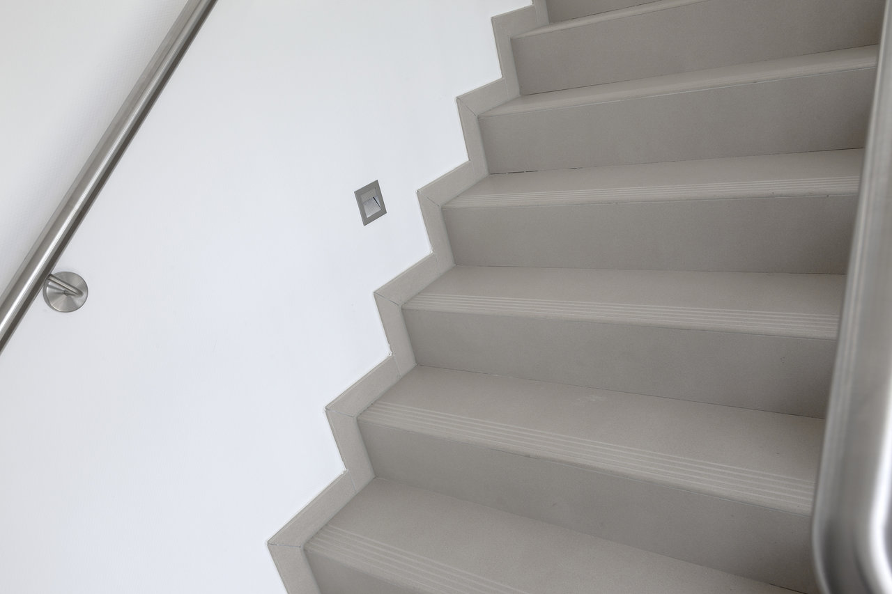 Modern tiled staircase with stainless steel railing and indirect lighting.