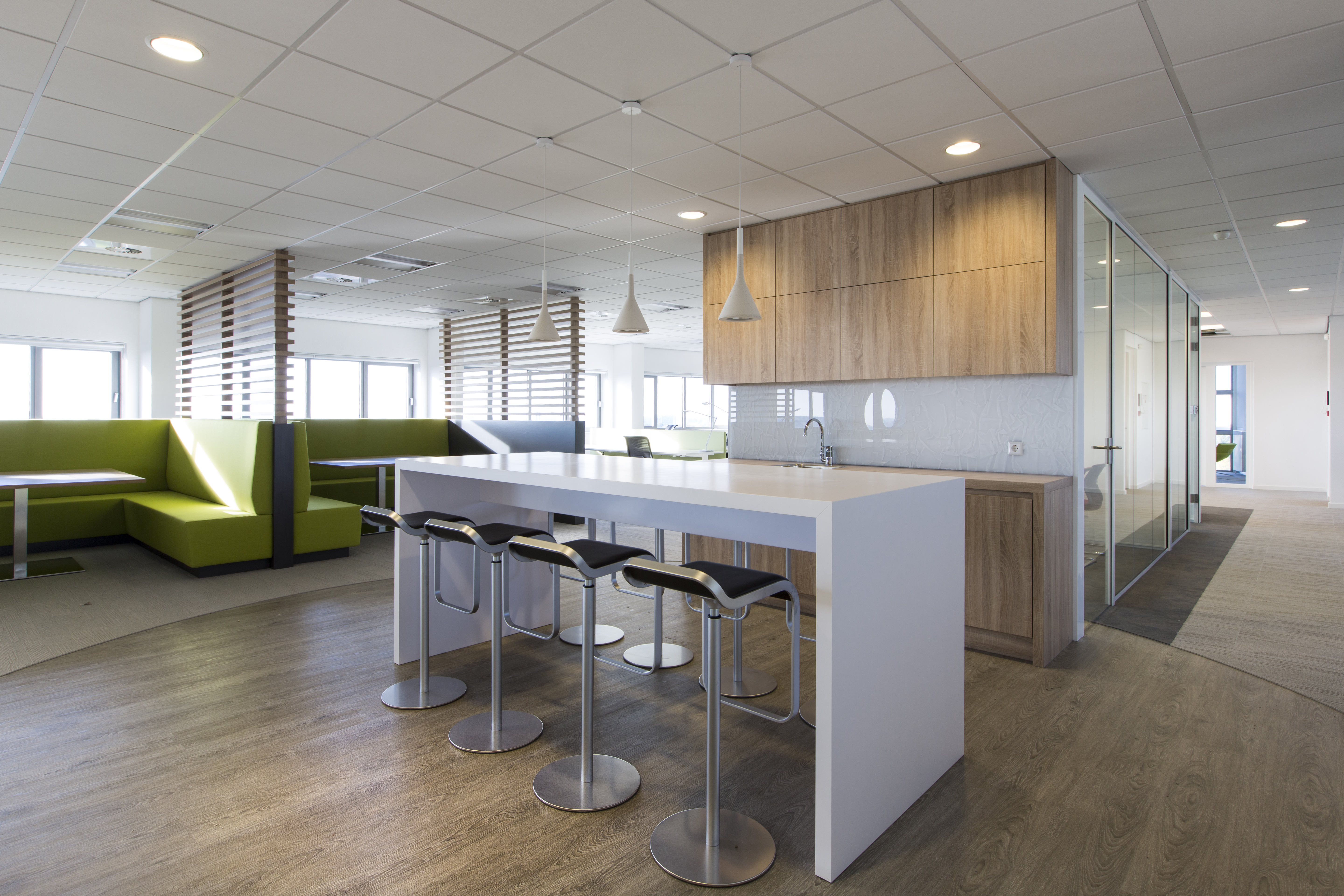 Modern office area with light wood-look tiles, kitchenette, and green benches.