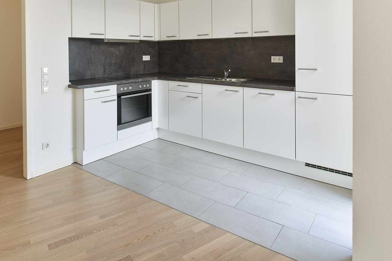 Modern kitchen with light grey floor tiles bordering a wooden floor.