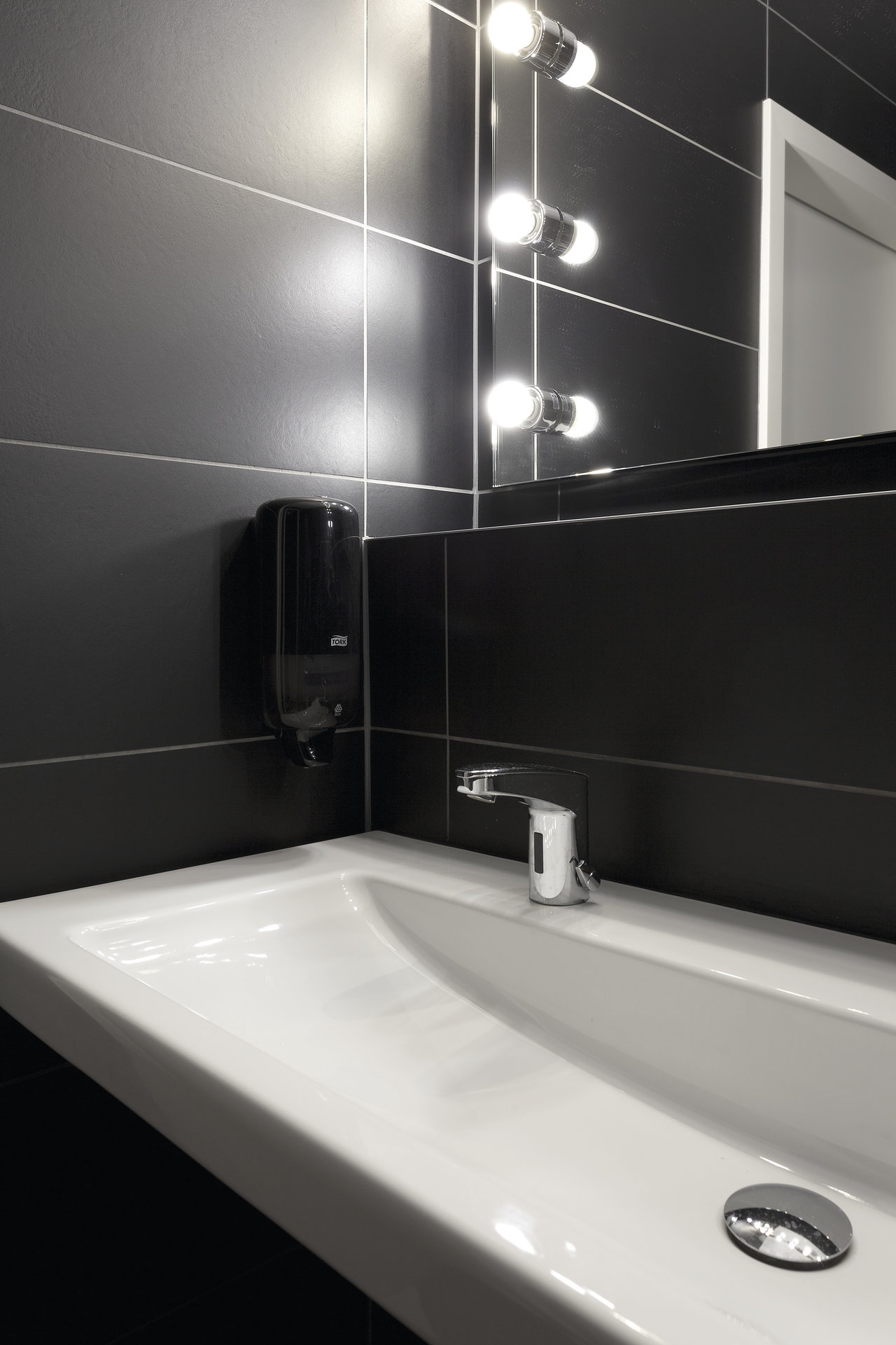 Black wall tiles in a modern bathroom with a white washbasin.