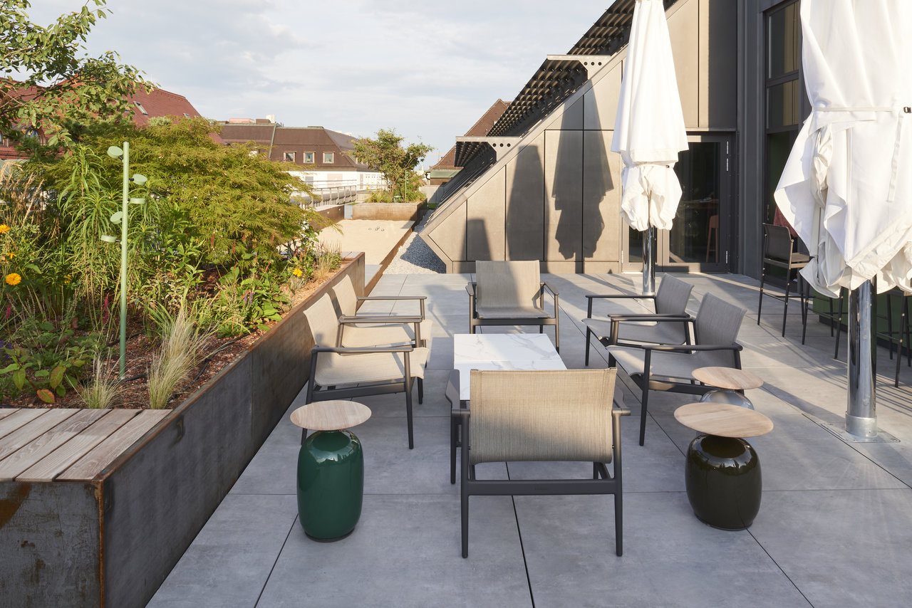 Modern roof terrace with light grey outdoor tiles, stylish furniture, and lush planting.
