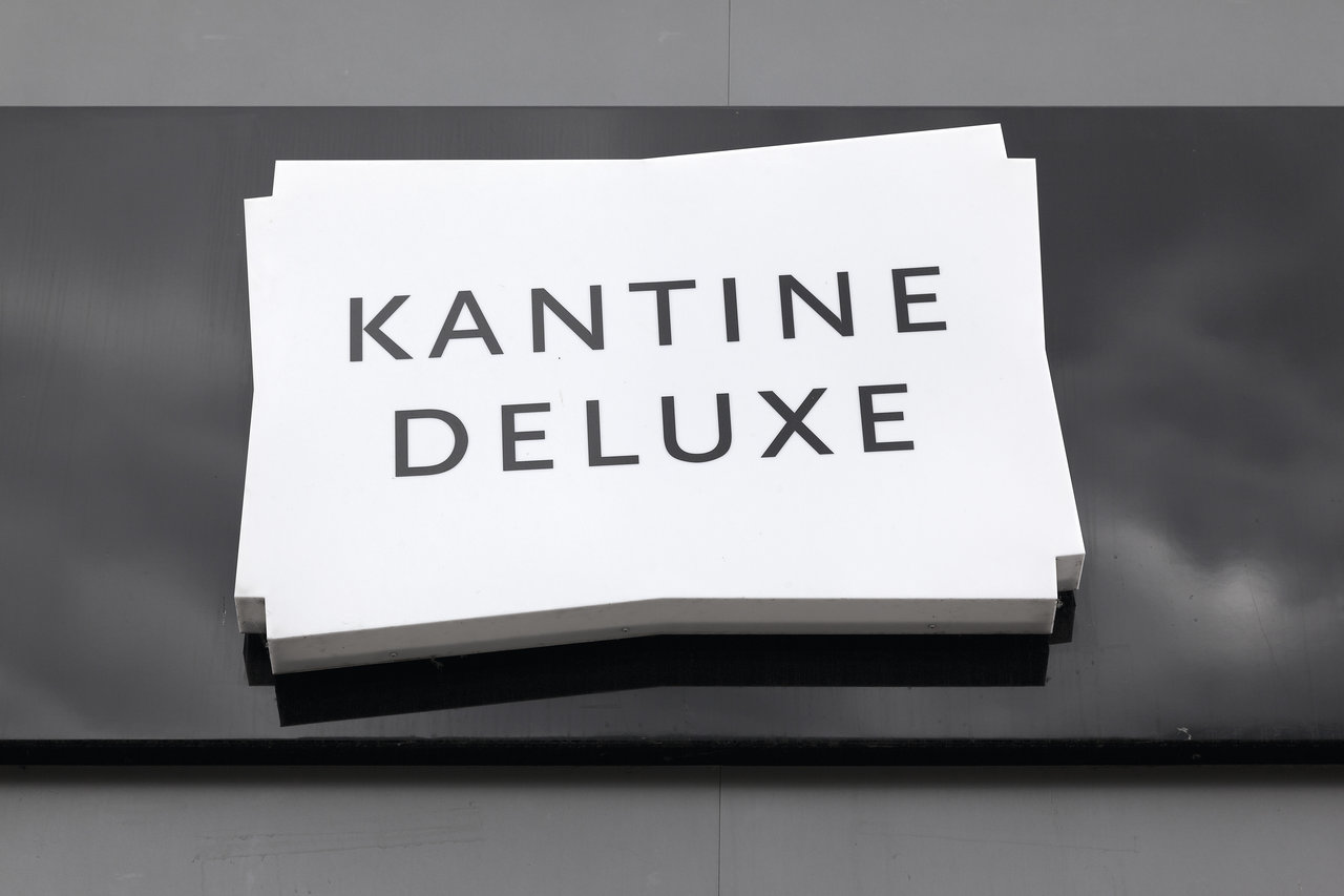 Modern sign "CANTEEN DELUXE" on dark tiled floor.