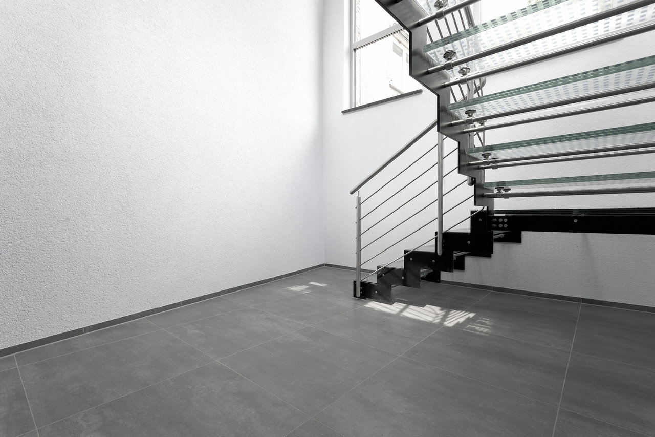High-quality grey porcelain tiles in a modern room with a metal staircase.