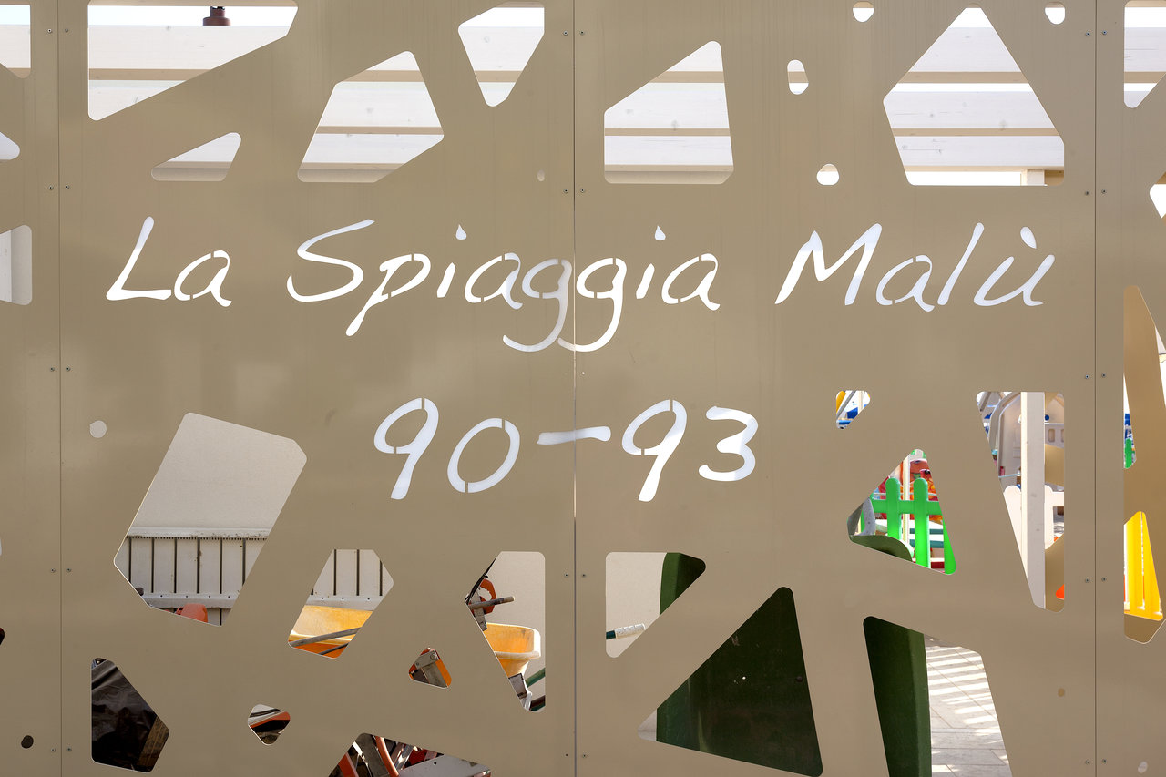 Decorative panel with "La Spiaggia Malù 90-93" lettering and openwork pattern.