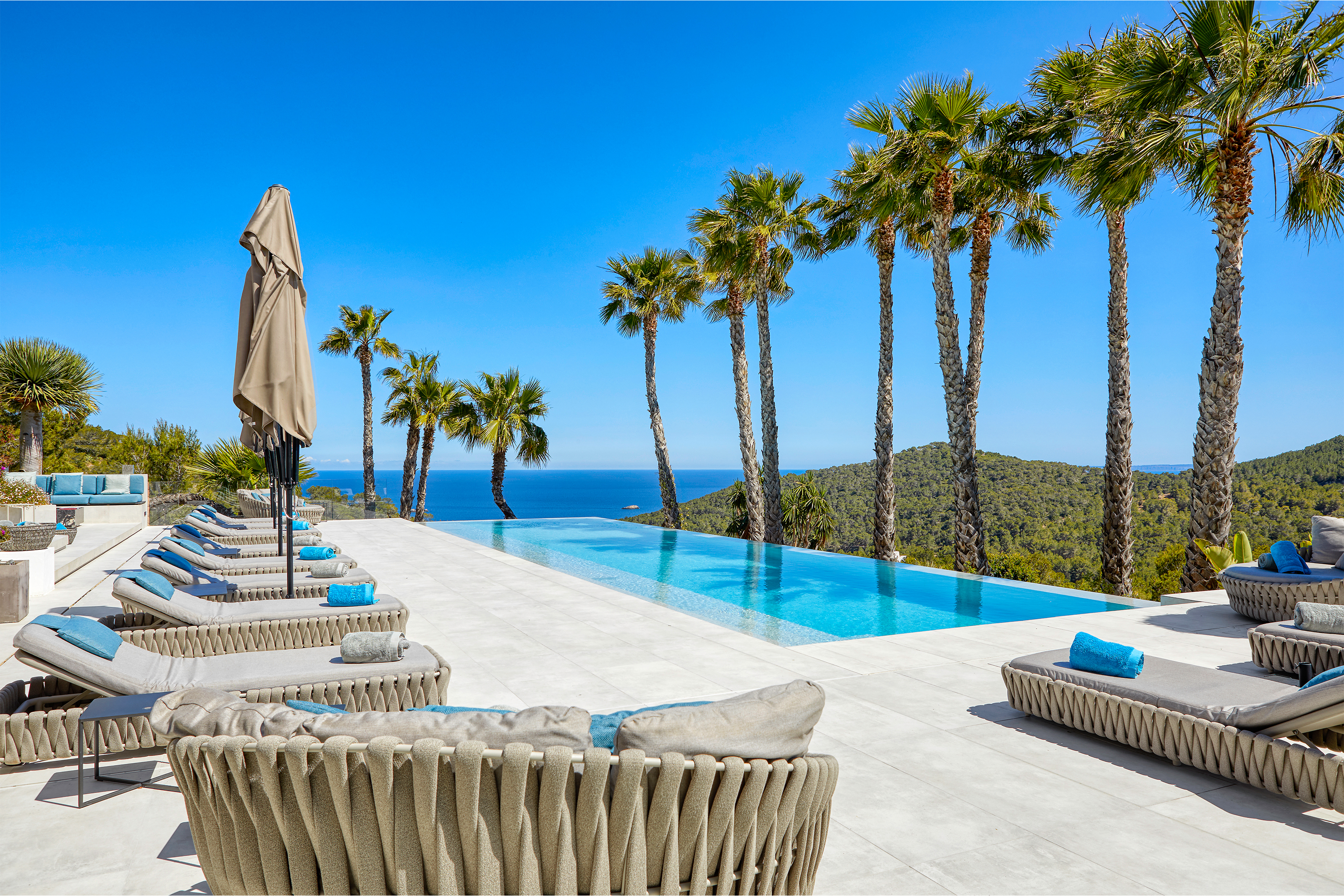 Luxurious pool area with light outdoor tiles, sea view under palm trees.
