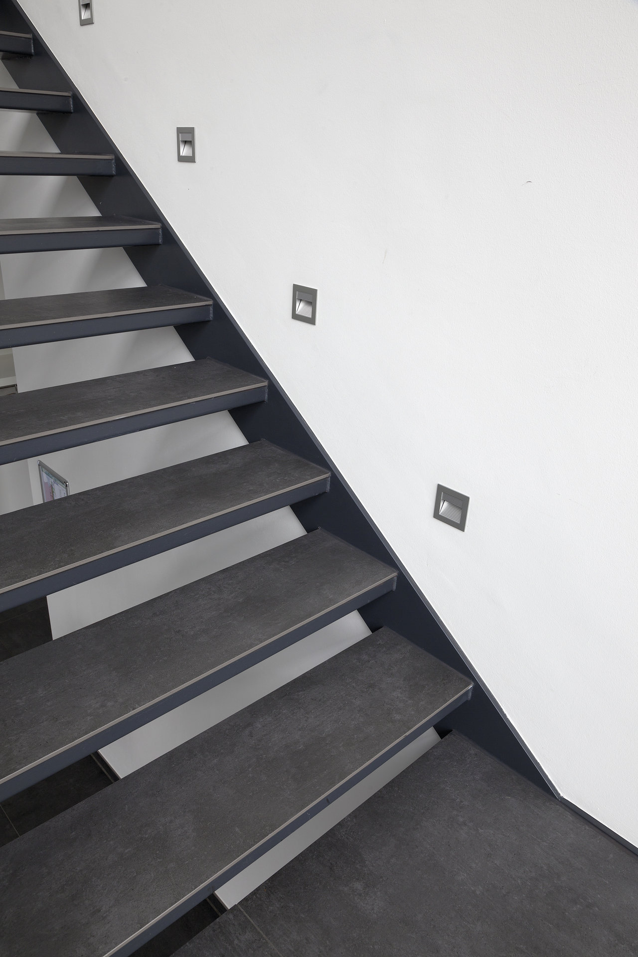 Stairs with anthracite tile steps and stylish wall lighting.