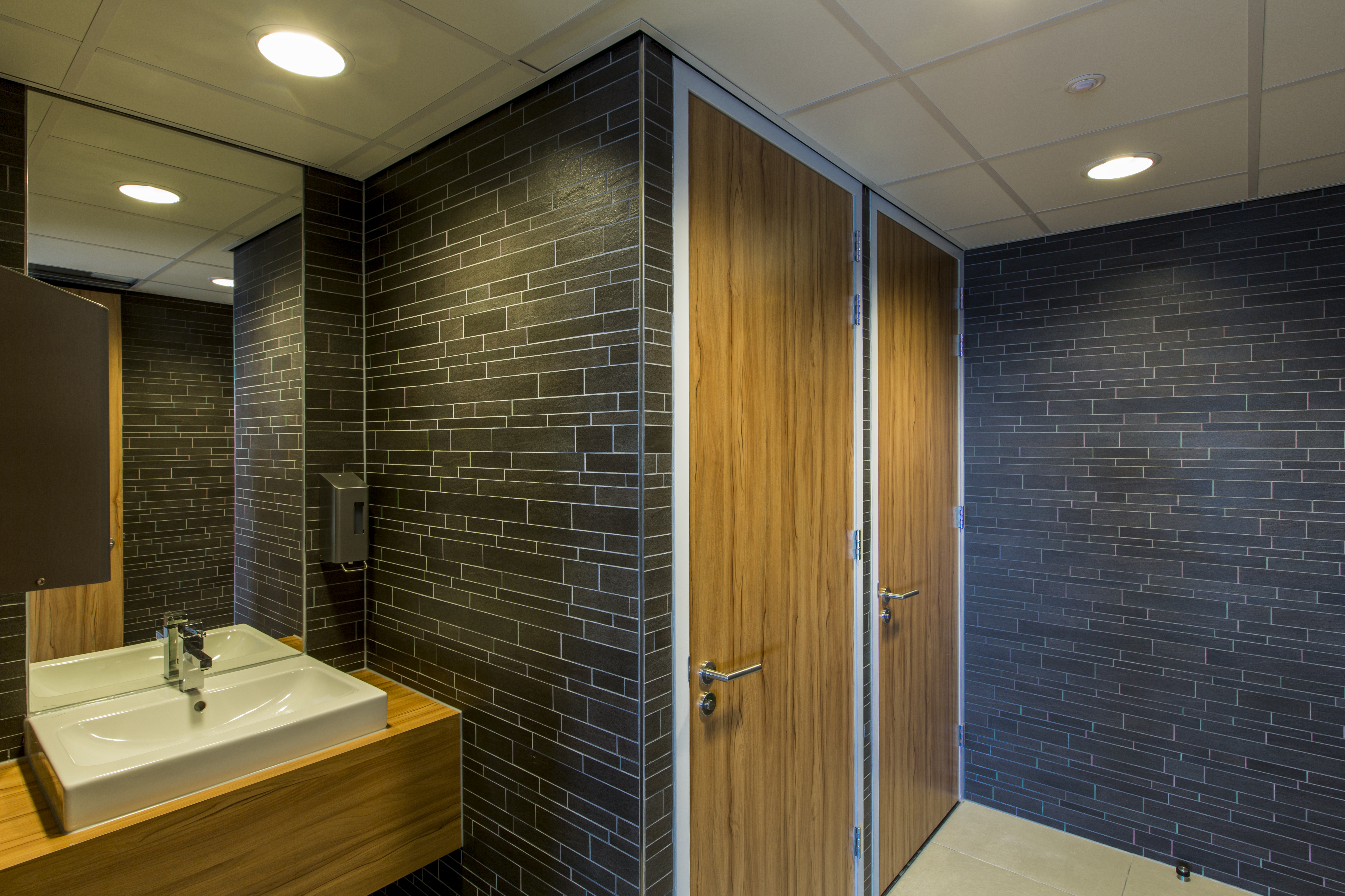 Dark slate effect wall tiles in a modern washroom with wooden doors and sink.