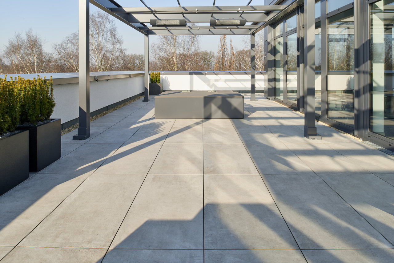 Modern roof terrace with light grey outdoor tiles and elegant pergola.