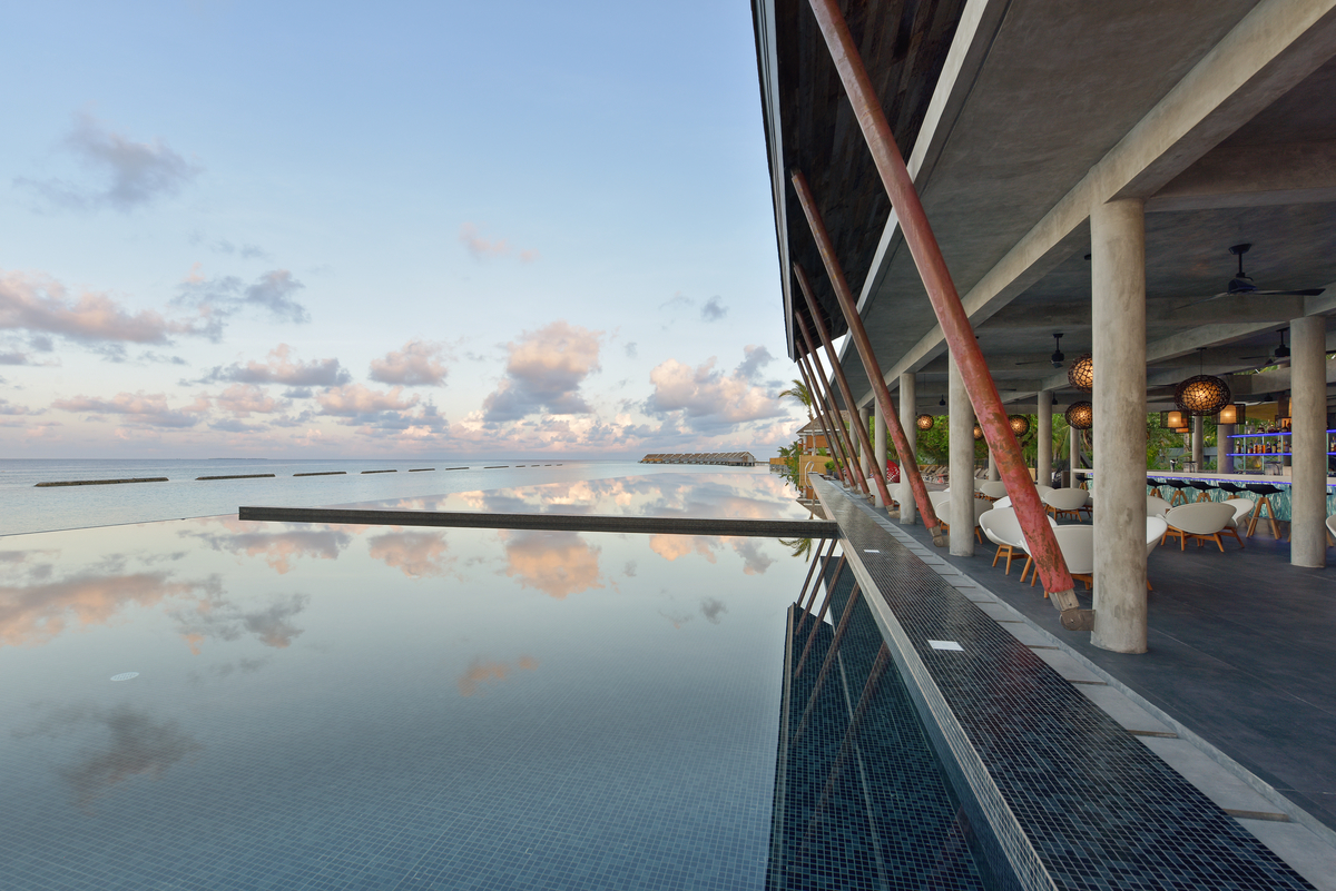 Infinity pool with mosaic tiles and elegant terrace with dark floor tiles by the sea.