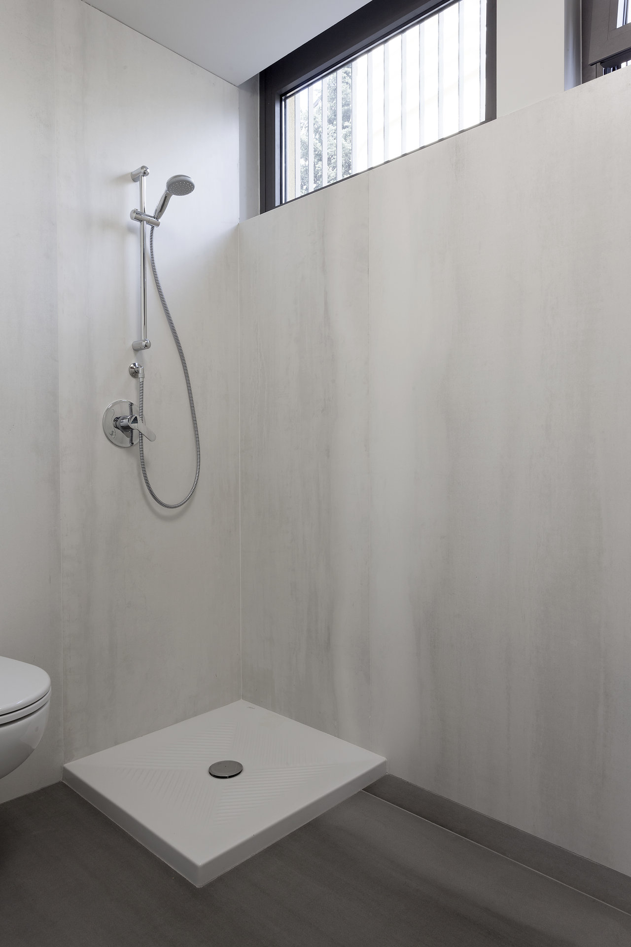 Modern bathroom with textured light wall tiles, dark floor, and white shower tray.