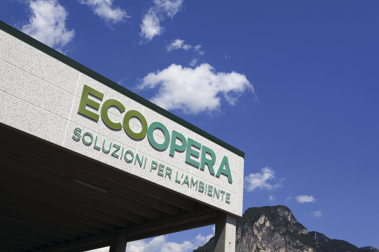 Building facade with ECOOPERA lettering and "Soluzioni per l'ambiente" against a mountain backdrop.
