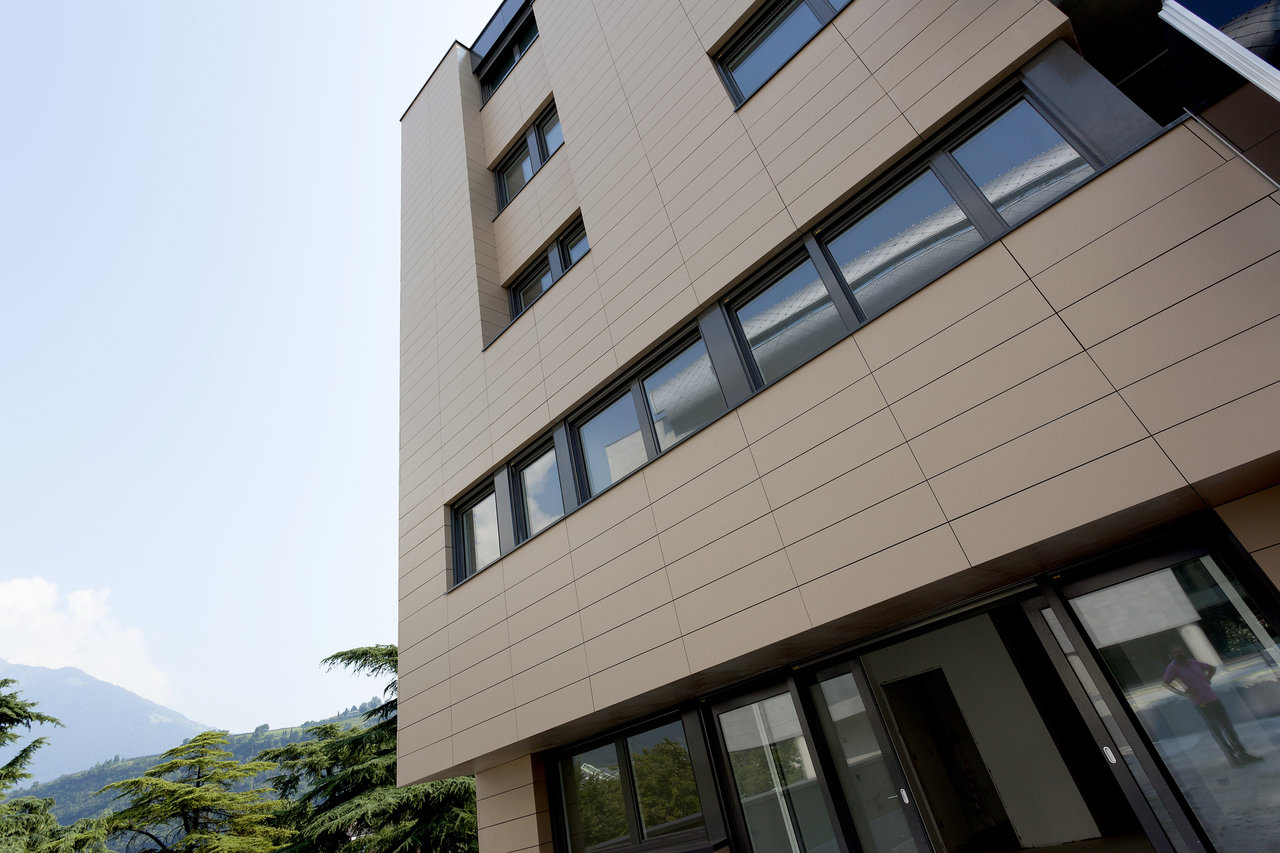 Modern building facade with beige outdoor tiles and large glass windows.