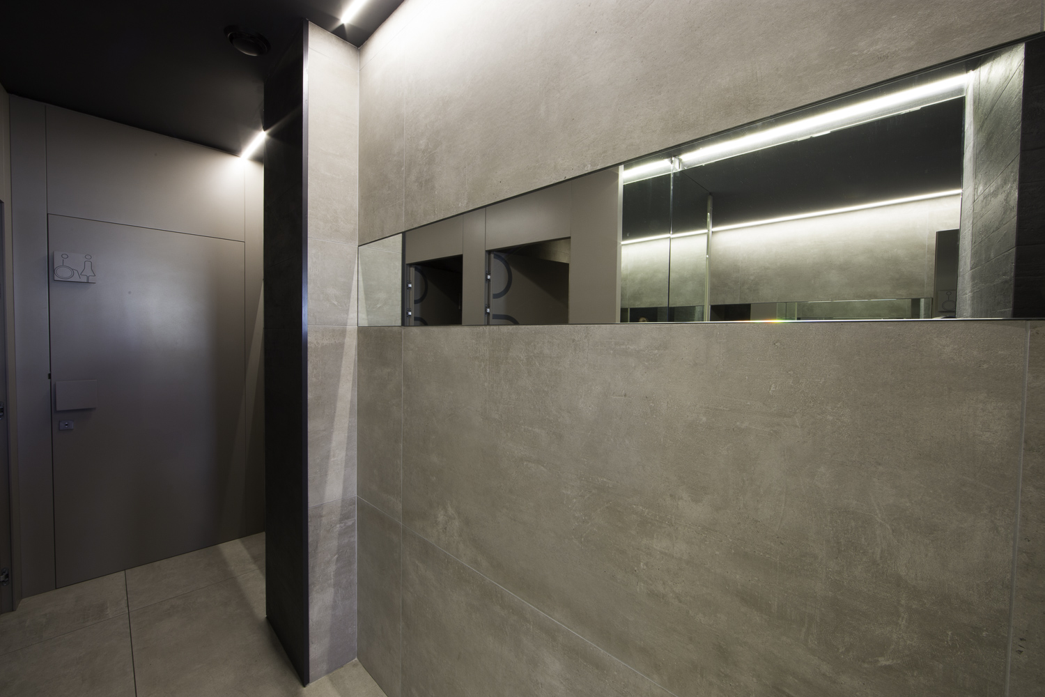 Grey concrete-effect wall and floor tiles in a modern hallway with indirect lighting.