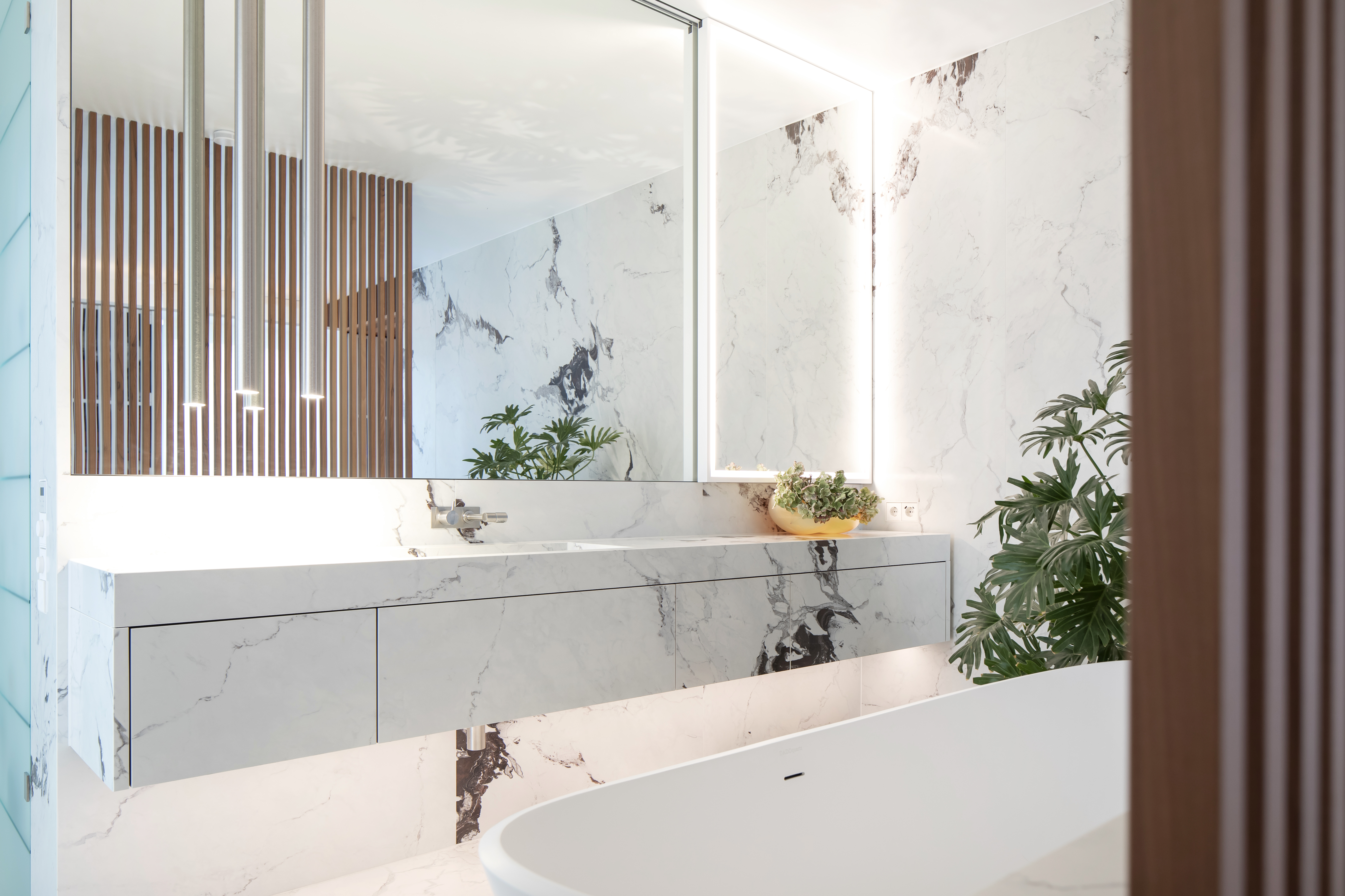 Bright bathroom with white marble-effect tiles, vanity unit, illuminated mirror, and bathtub.