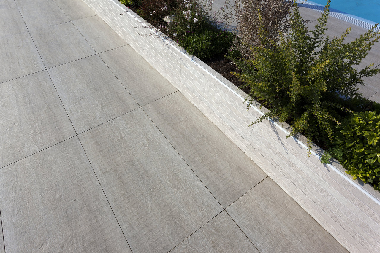 Light outdoor tiles with subtle wood structure on a modern poolside terrace.