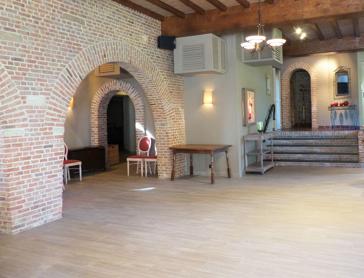 Light wood-effect tiles in a spacious room with brick arches and wooden beams.